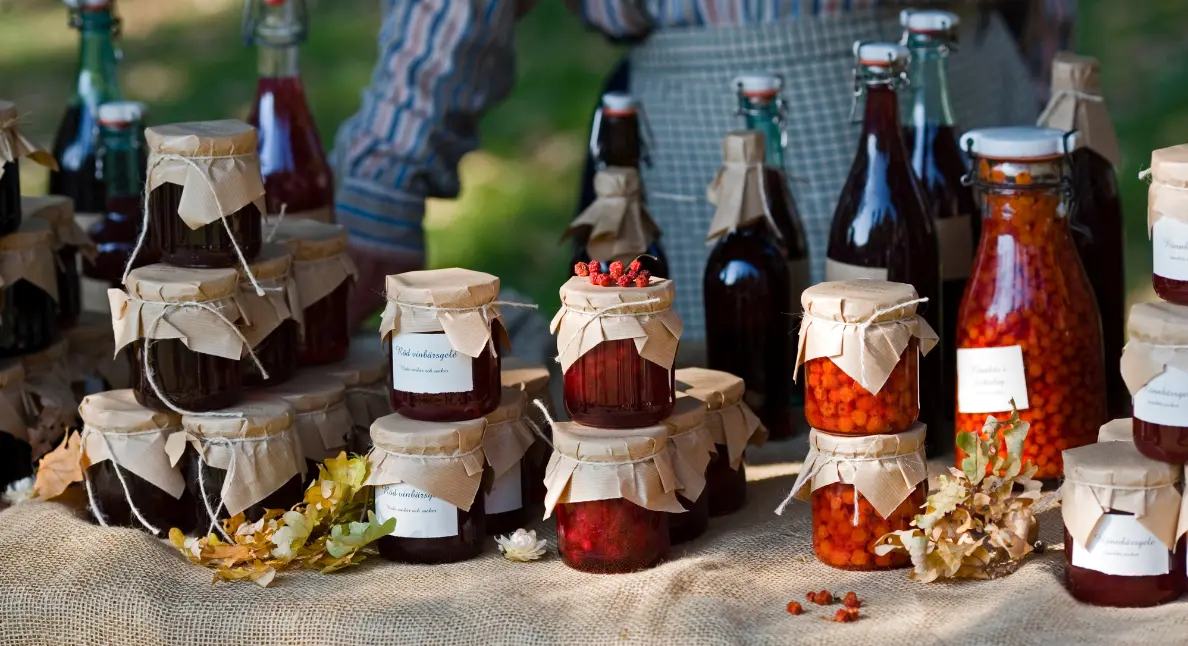 Artisanal goods displayed in glass jars and bottles at a rustic outdoor market stall.