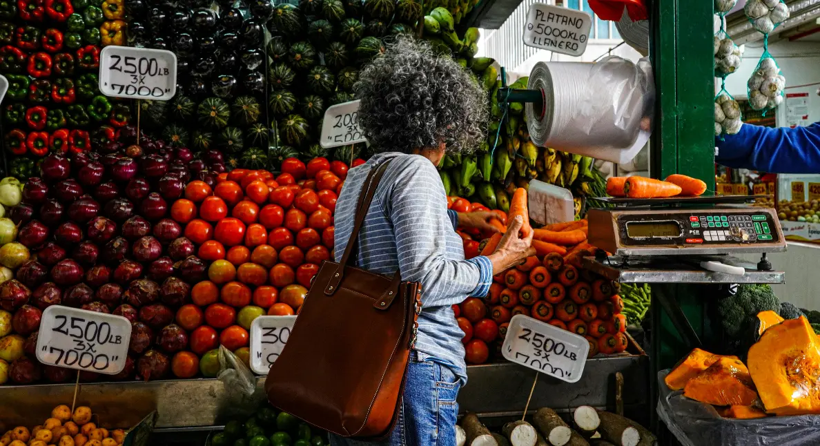 Best local foods chosen by a shopper at a colorful produce stand filled with fresh carrots, tomatoes, and plantains.