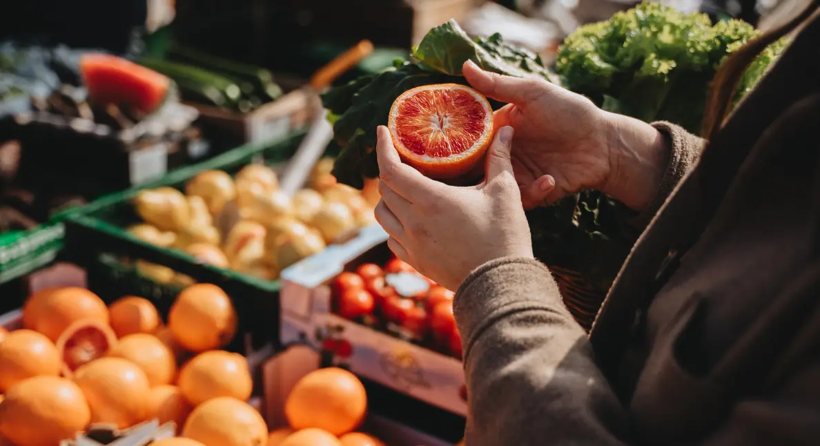 Fresh produce including citrus fruits and leafy greens being inspected at a local outdoor market.