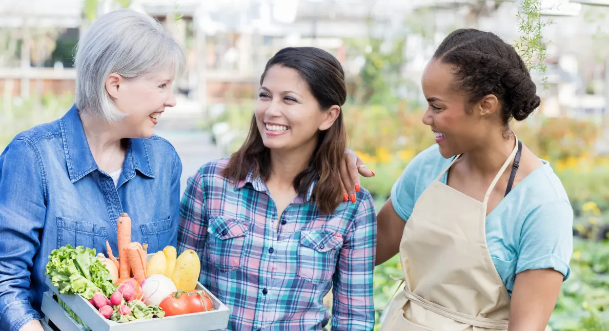 Local farmers sharing smiles while holding a box of fresh vegetables at a community market.