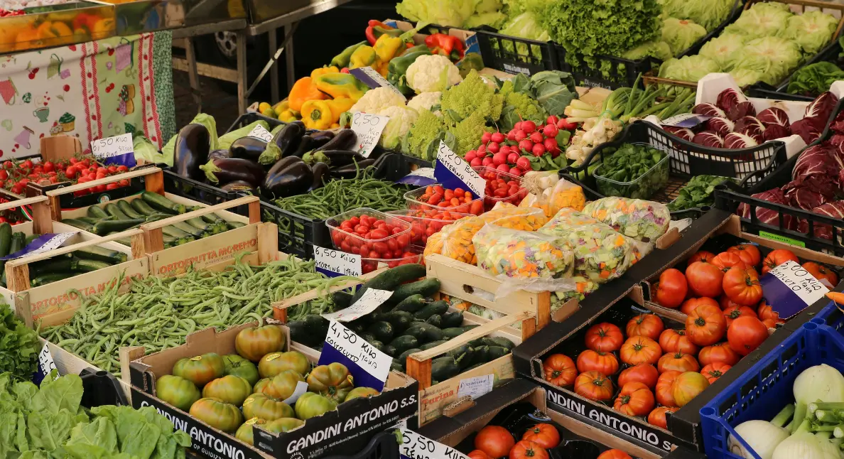 Local makers displaying colorful fresh vegetables and greens at an outdoor produce market.