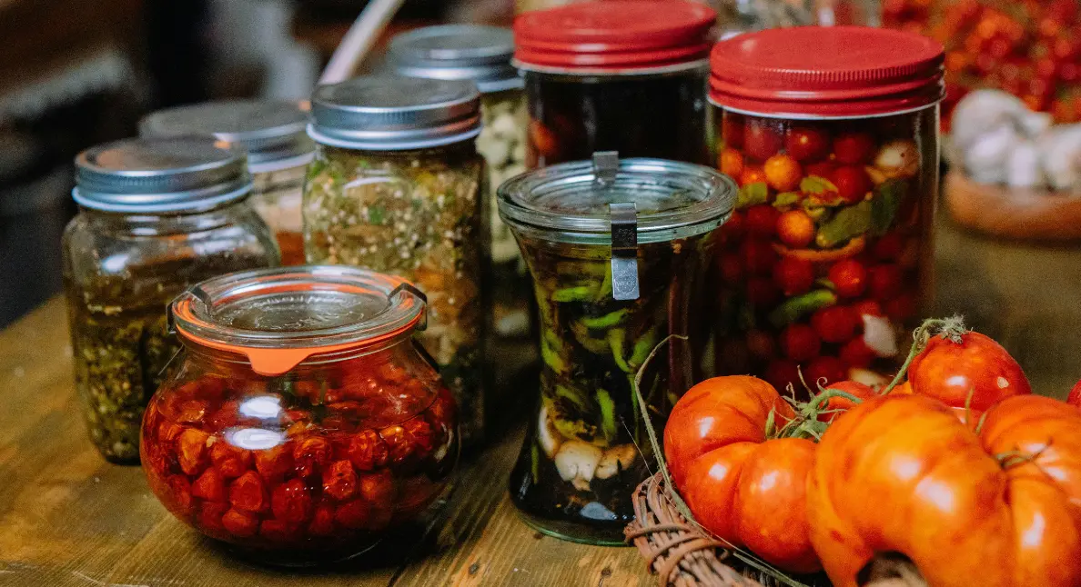 Small businesses offering assorted pickled vegetables and preserves in jars alongside fresh tomatoes.