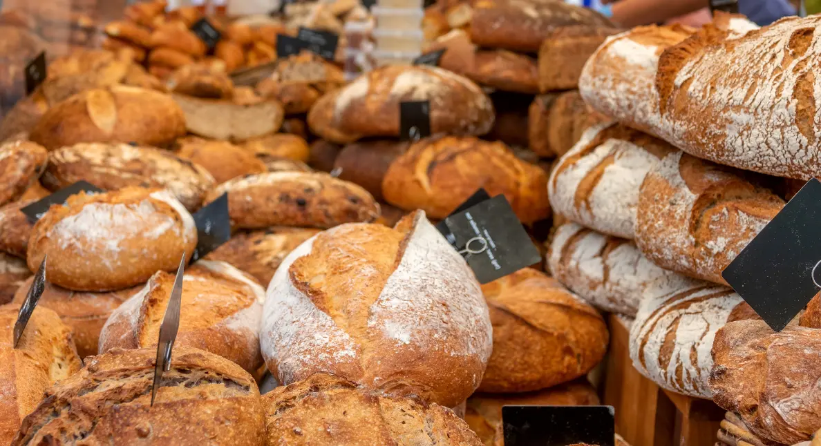 Small-batch baking goods and fresh vegetables fill a reusable tote at a local outdoor market.