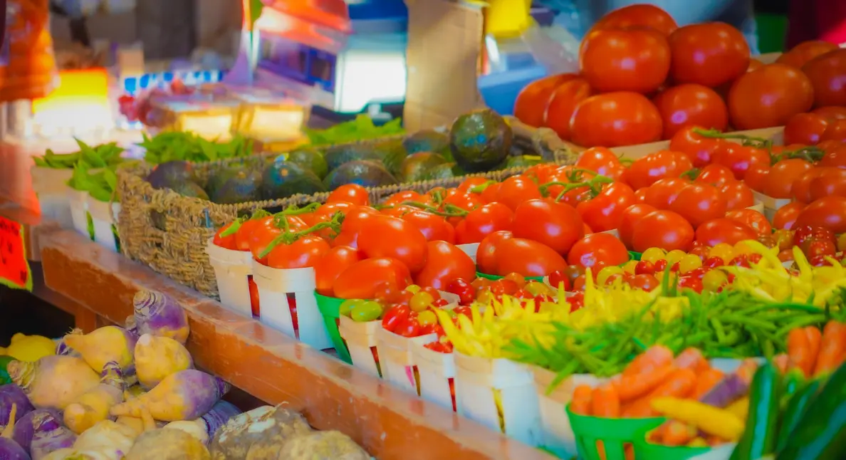 Good local food displayed in baskets filled with tomatoes, peppers, and other vibrant vegetables at a market stall.
