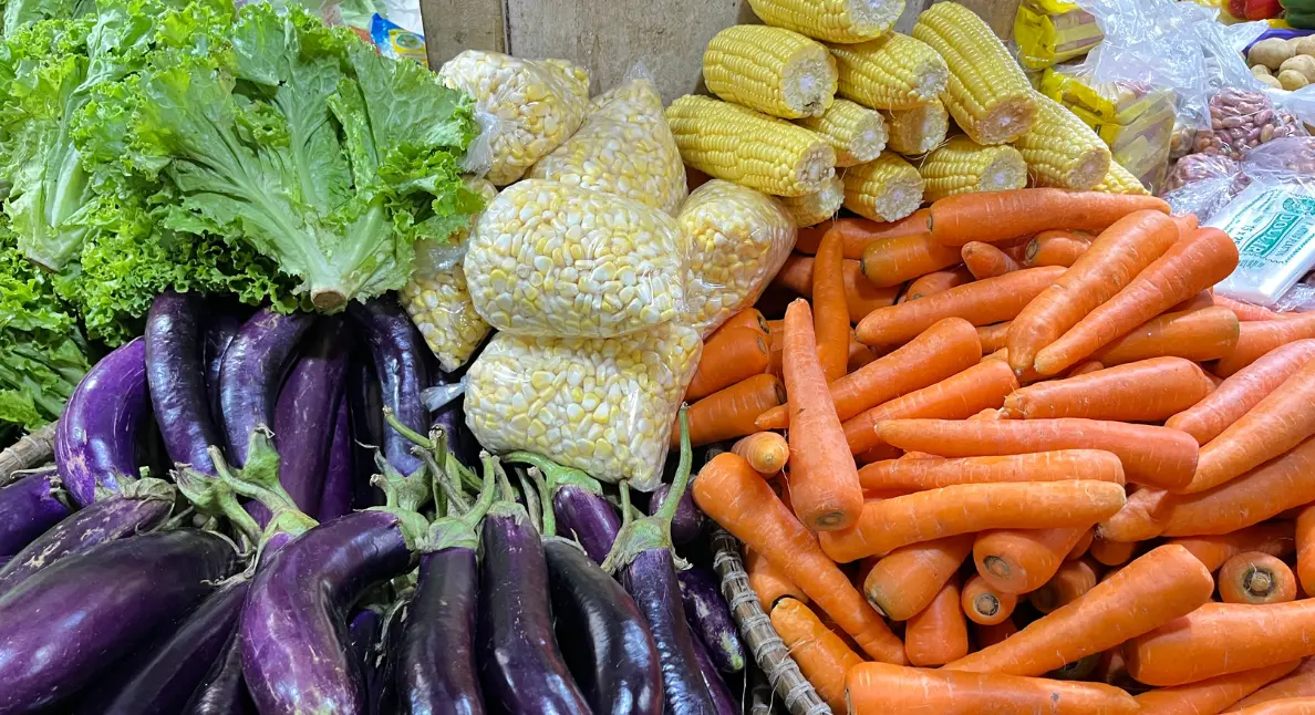 Handmade food movement represented by fresh vegetables including corn, eggplant, lettuce, and carrots at a local market stall.