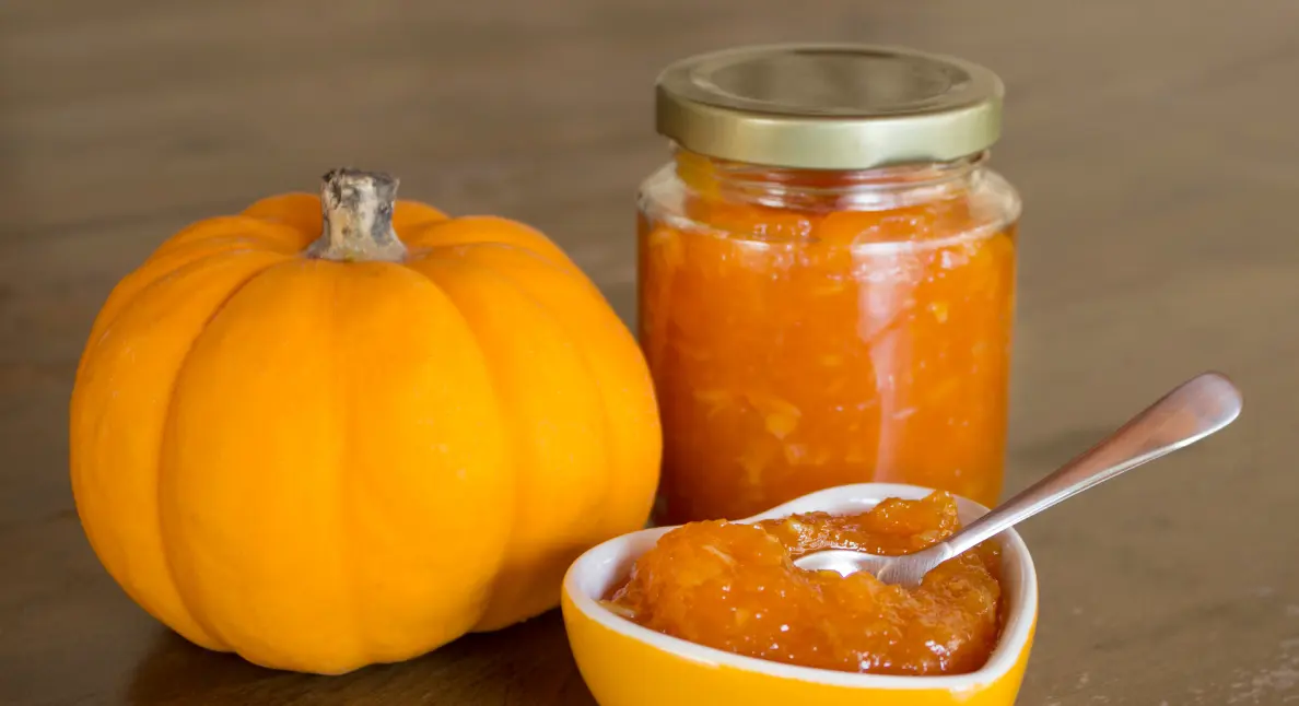 Homemade fruit preserves featuring pumpkin jam in a jar beside a whole pumpkin.