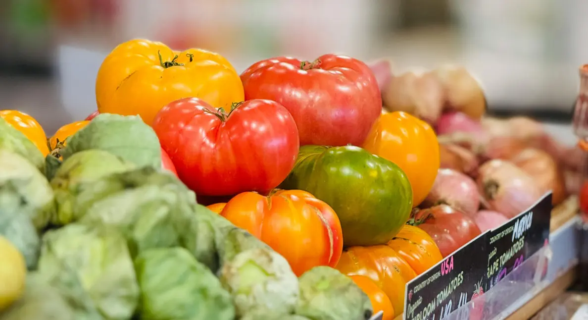 Local food marketplace showcasing heirloom tomatoes and tomatillos neatly displayed at a grocery stand.