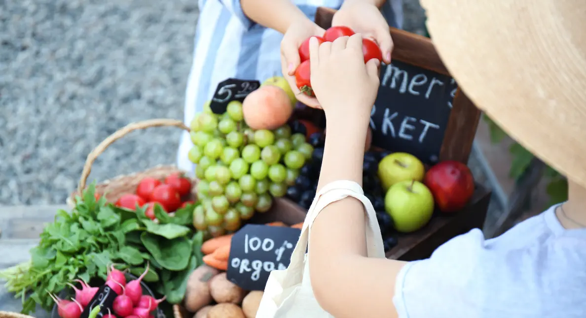 Local food producers selling fresh organic fruits and vegetables at a small farmers market stand.