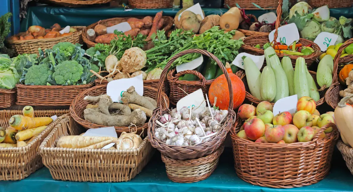 Local products arranged in wicker baskets including garlic, apples, and root vegetables at a farmers market.