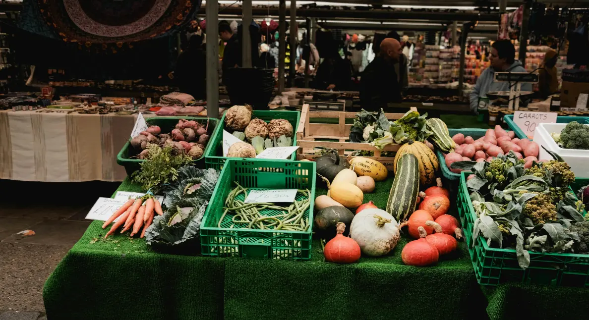Organic food stores showcasing fresh root vegetables, squash, leafy greens, and carrots arranged in crates at an indoor market stall.
