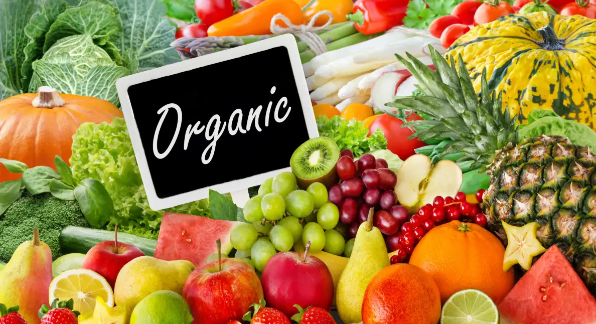 Premium foods displayed in a vibrant assortment of fresh fruits and vegetables surrounding a sign labeled organic at a market stand.