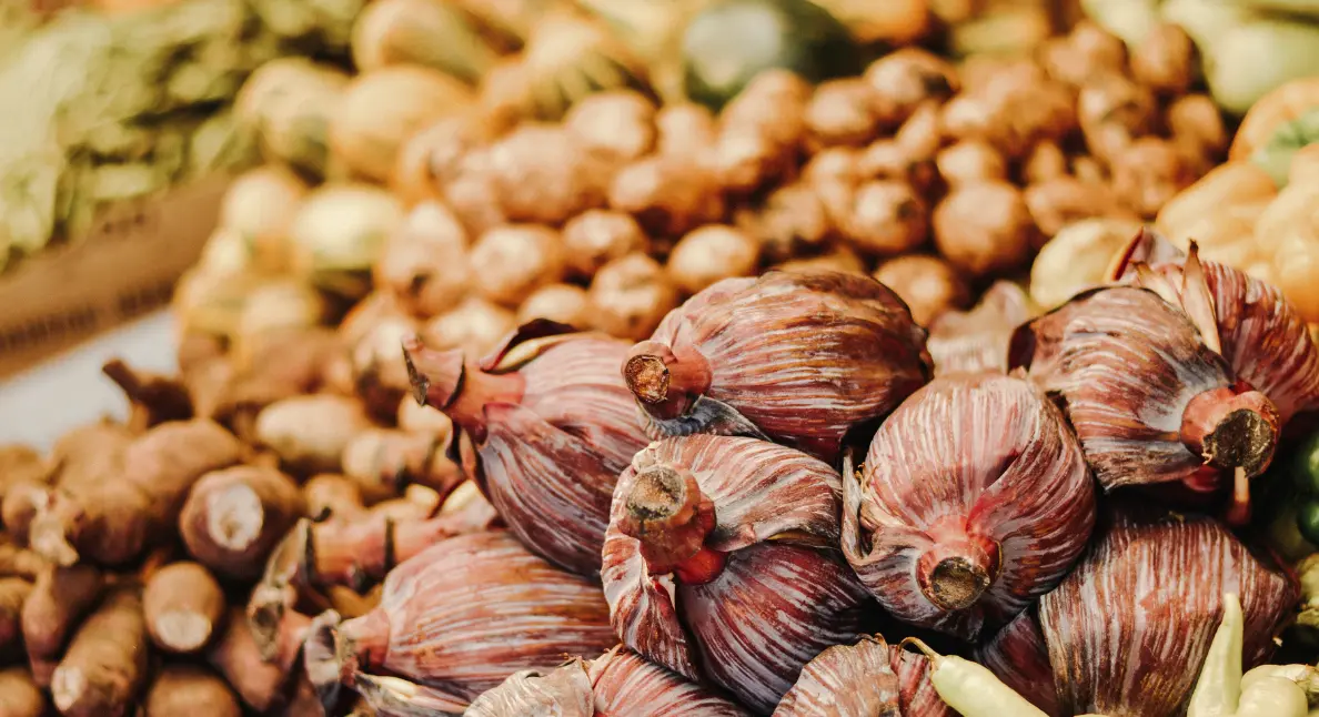 Small-batch food like banana blossoms and root vegetables stacked at a rustic farmer's market display.