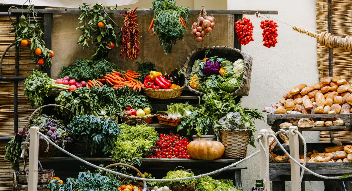 A rustic outdoor market stall overflowing with fresh produce, including hanging herbs, root vegetables, leafy greens, and artisan bread. A rustic outdoor market stall overflowing with fresh produce, including hanging herbs, root vegetables, leafy greens, and artisan bread.