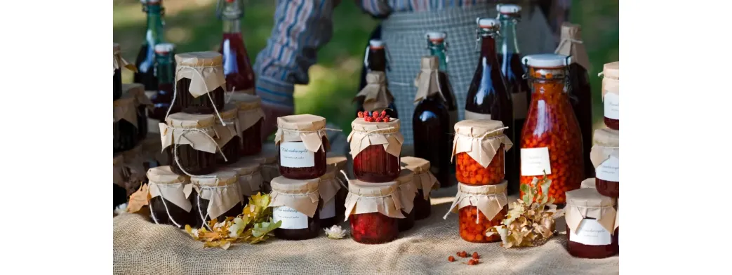 Artisanal goods displayed in glass jars and bottles at a rustic outdoor market stall.