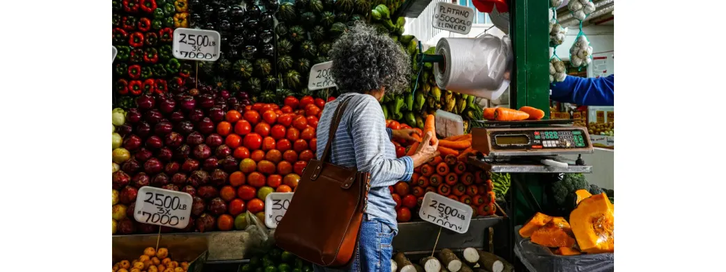 Best local foods chosen by a shopper at a colorful produce stand filled with fresh carrots, tomatoes, and plantains.