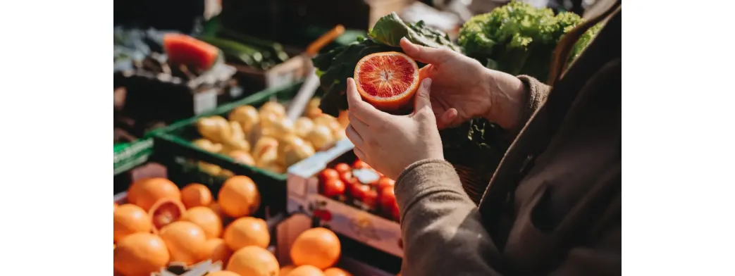 Fresh produce including citrus fruits and leafy greens being inspected at a local outdoor market.