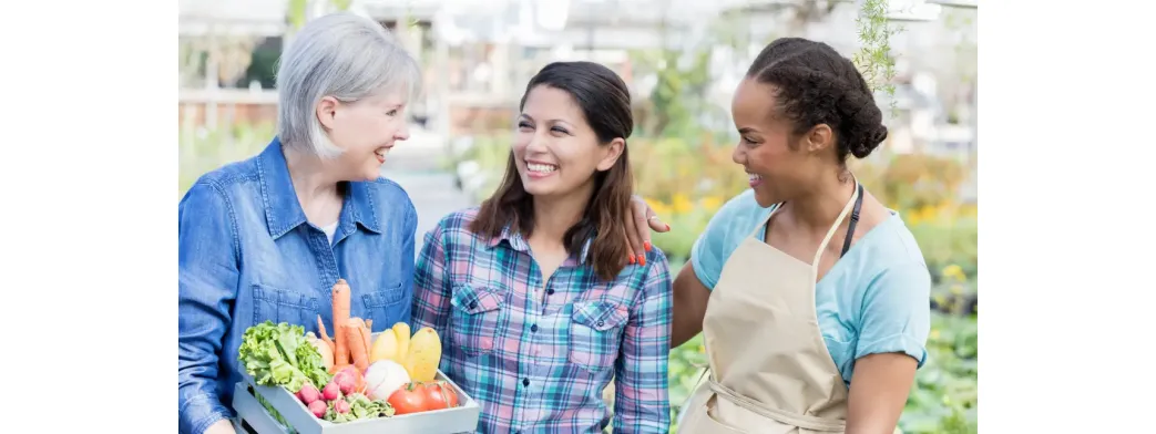 Local farmers sharing smiles while holding a box of fresh vegetables at a community market.