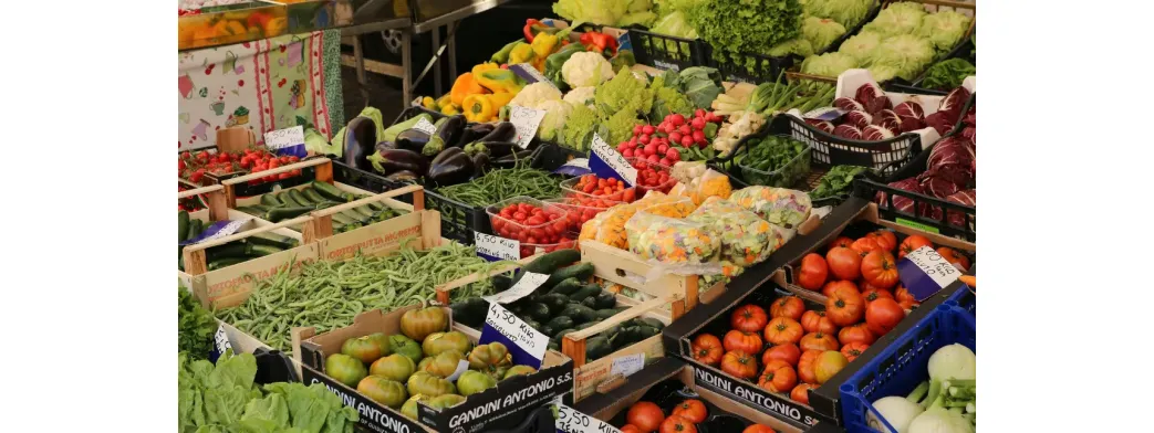 Local makers displaying colorful fresh vegetables and greens at an outdoor produce market.