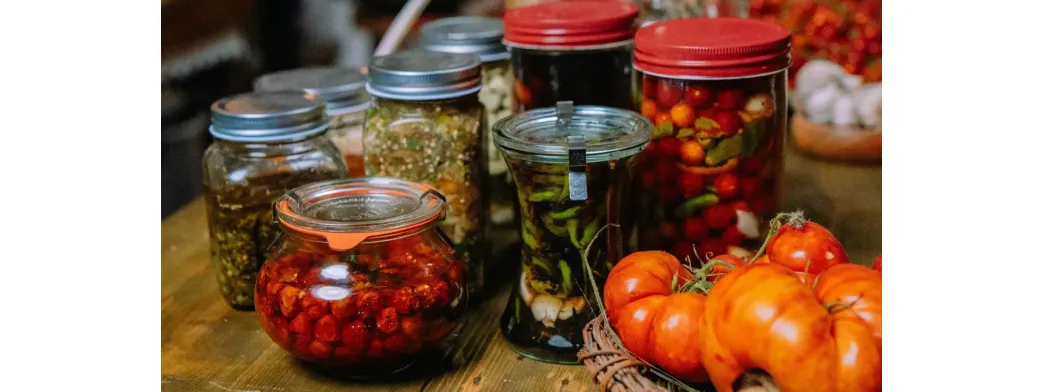 Small businesses offering assorted pickled vegetables and preserves in jars alongside fresh tomatoes.