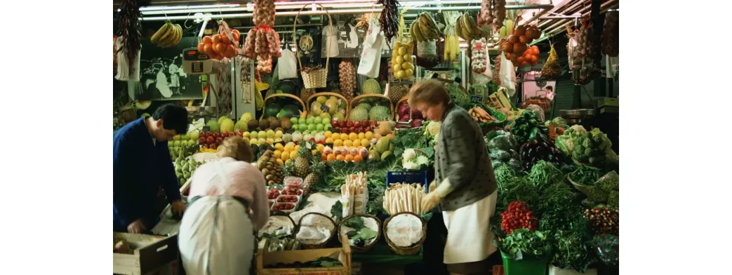 Support local farmers by shopping at a colorful produce stall staffed by market vendors and filled with fresh fruits and vegetables.