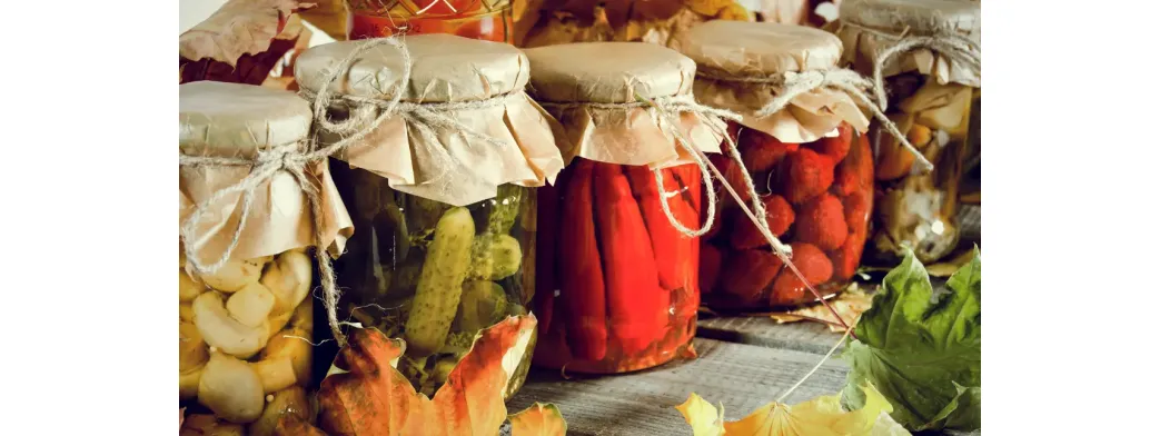 Sustainable products like pickled vegetables and fruits preserved in reusable glass jars with paper tops.