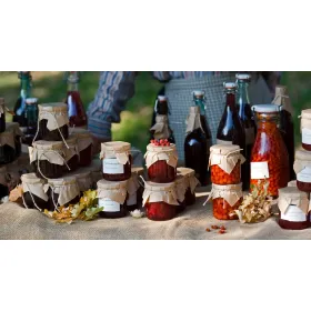 Artisanal goods displayed in glass jars and bottles at a rustic outdoor market stall.