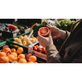 Fresh produce including citrus fruits and leafy greens being inspected at a local outdoor market.