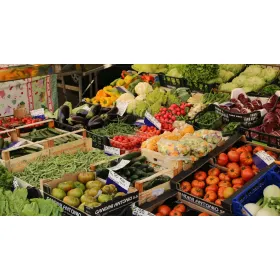Local makers displaying colorful fresh vegetables and greens at an outdoor produce market.