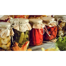 Sustainable products like pickled vegetables and fruits preserved in reusable glass jars with paper tops.
