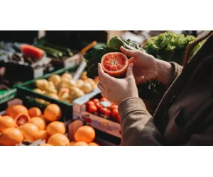 Fresh produce including citrus fruits and leafy greens being inspected at a local outdoor market.