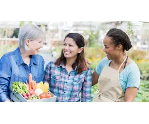 Local farmers sharing smiles while holding a box of fresh vegetables at a community market.