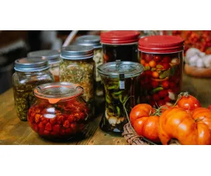 Small businesses offering assorted pickled vegetables and preserves in jars alongside fresh tomatoes.