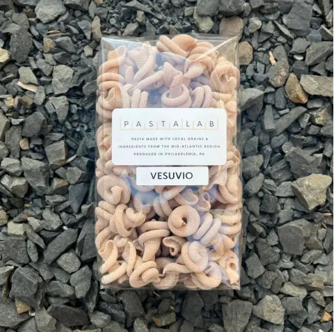 Vesuvio spelt pasta in a clear Pasta Lab bag with a label on gray gravel stones.
