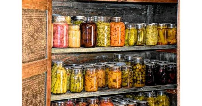 Pantry ingredients like pasta, legumes, and dried goods neatly stored in glass jars on a backlit shelf.