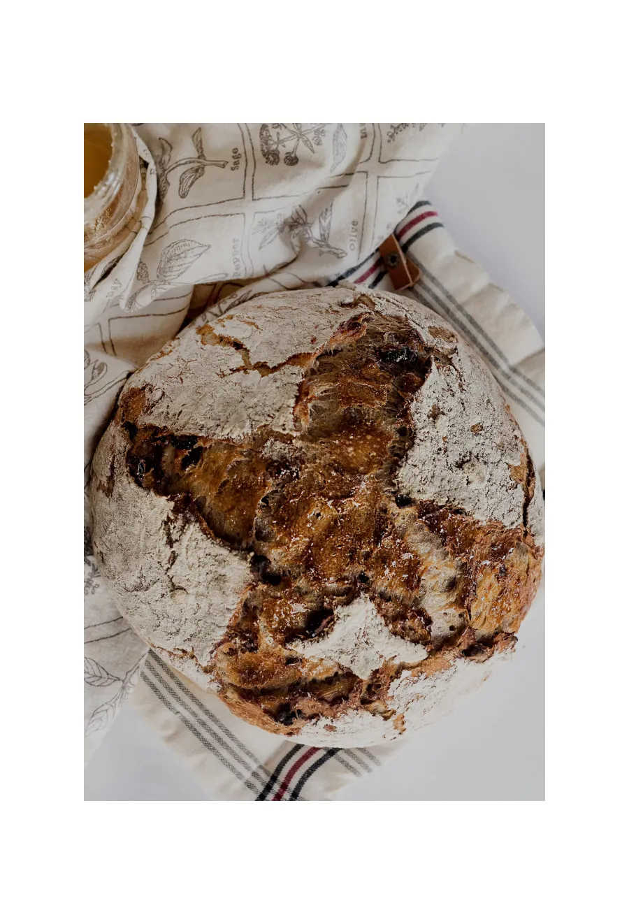 Artisan bread with a rustic crust sits on a linen cloth near a jar of honey.