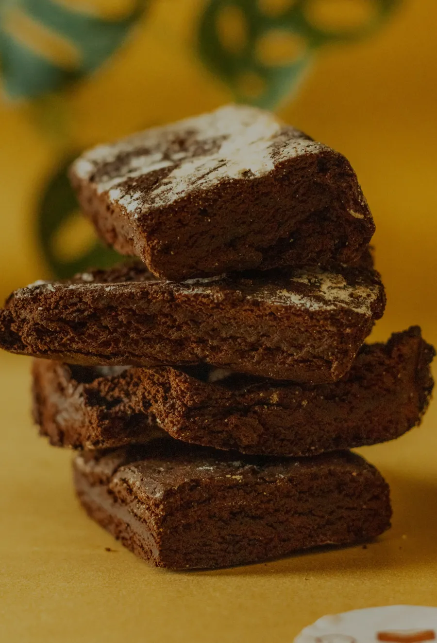 Brownies stacked on a yellow surface, showing rich, fudgy texture and a dusting of powdered sugar.