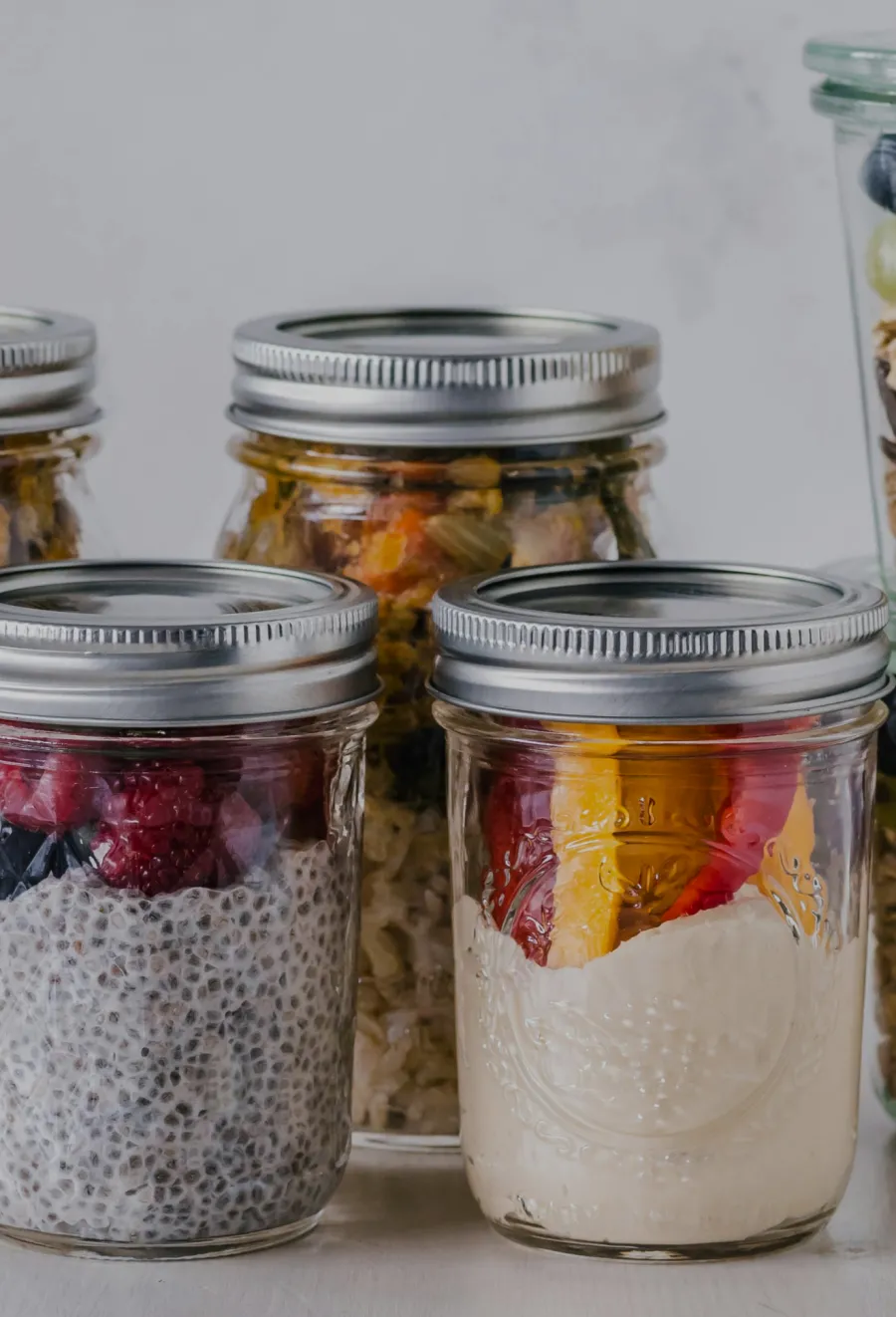 Canned goods in mason jars, including chia pudding and fruit parfaits, arranged on a white table.