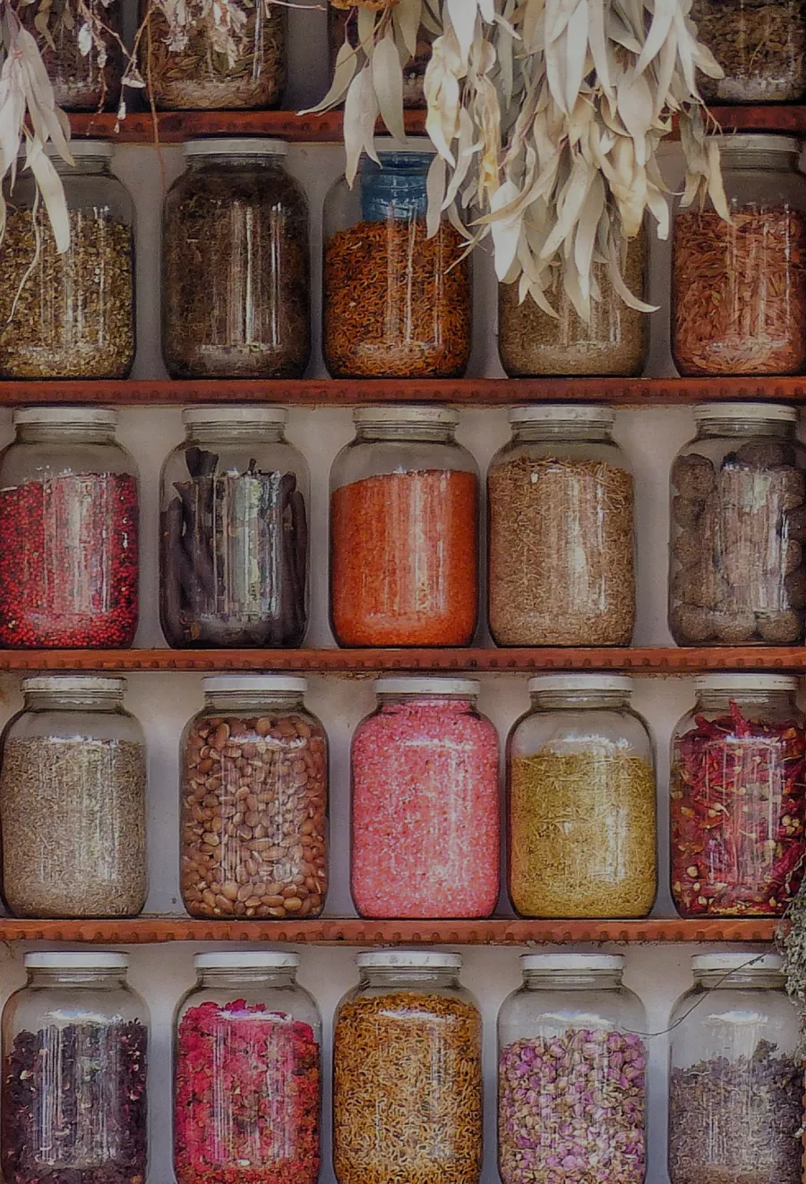Bulk spices stored in glass jars on wooden shelves, showcasing a colorful variety of herbs and seasonings.