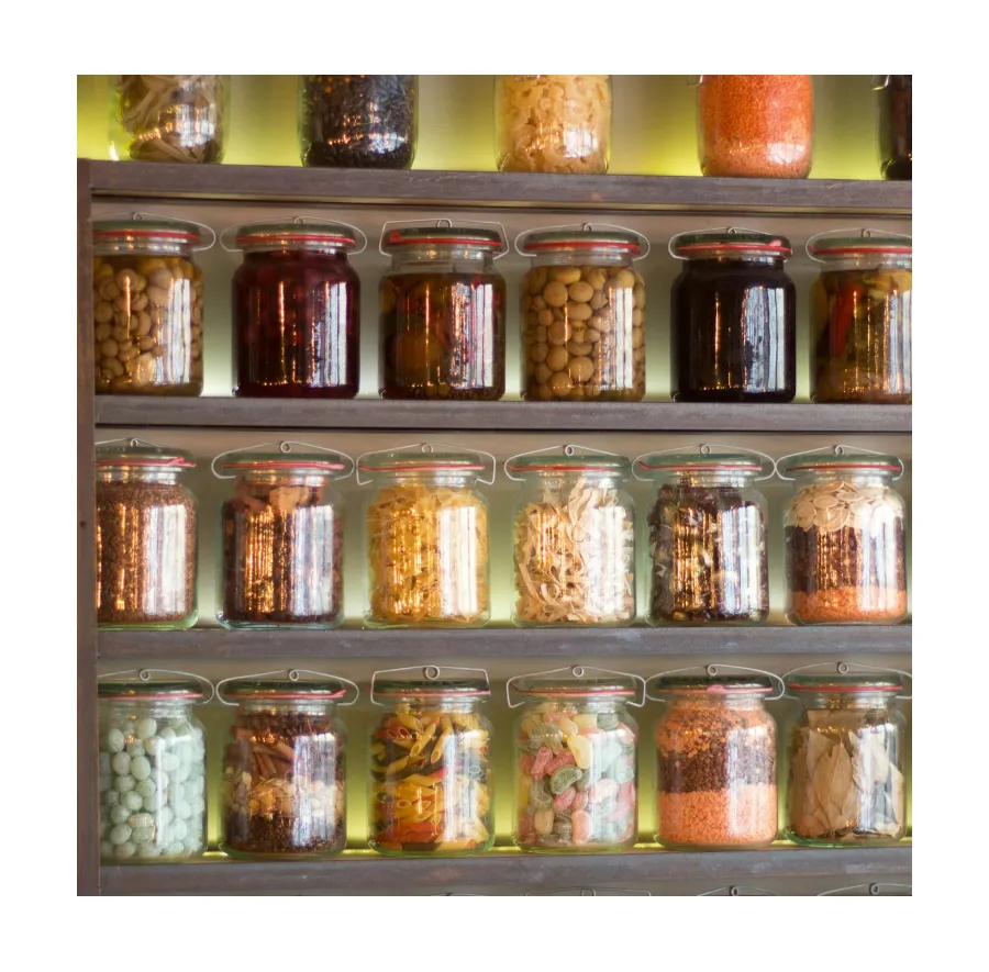 Pantry ingredients like pasta, legumes, and dried goods neatly stored in glass jars on a backlit shelf.